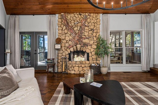 living room featuring a stone fireplace, a wealth of natural light, dark hardwood / wood-style flooring, and wooden ceiling