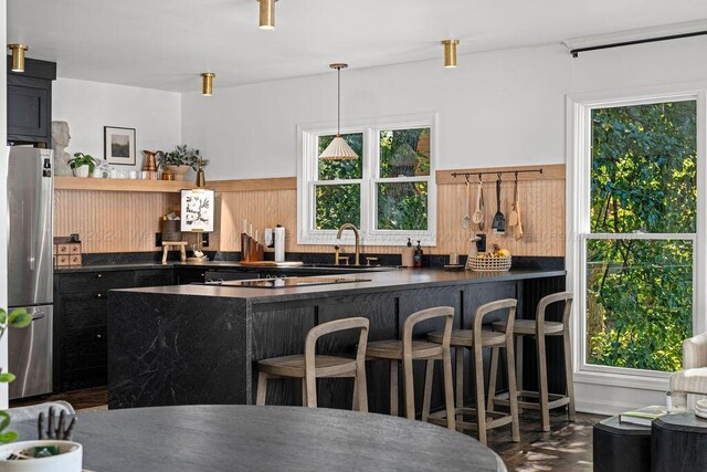 kitchen featuring hanging light fixtures, sink, a kitchen bar, kitchen peninsula, and stainless steel refrigerator