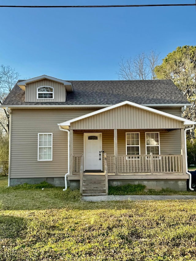 view of front of property featuring covered porch, a shingled roof, and a front lawn