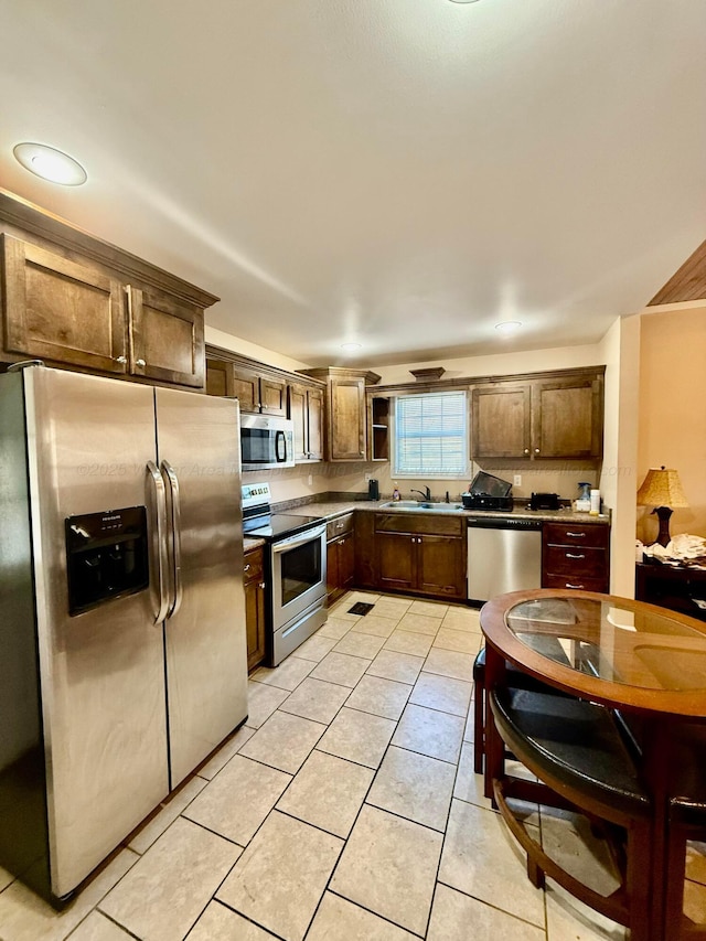 kitchen with light tile patterned floors, dark brown cabinetry, appliances with stainless steel finishes, and a sink