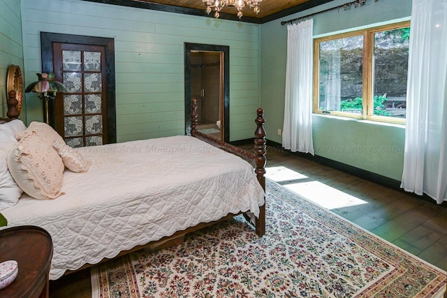 bedroom featuring wood walls, dark wood-type flooring, and a chandelier