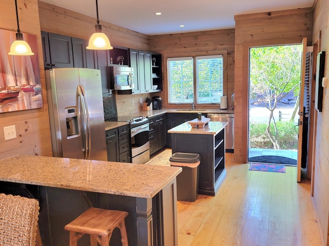 kitchen with a breakfast bar area, stainless steel appliances, a center island, light stone countertops, and pendant lighting