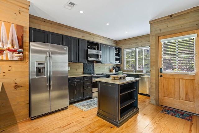 kitchen with stainless steel appliances, wood walls, light stone countertops, and a center island