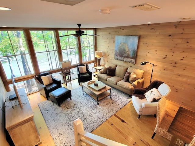 living room featuring light wood-type flooring, wood walls, ceiling fan, and plenty of natural light