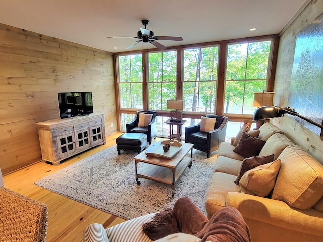 living room featuring ceiling fan, light hardwood / wood-style flooring, and wooden walls