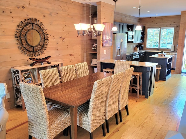 dining area with a notable chandelier, light wood-type flooring, and wooden walls