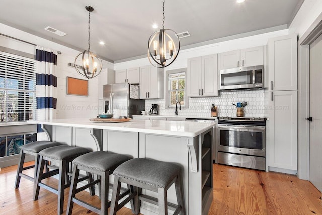 kitchen featuring hanging light fixtures, a kitchen bar, a kitchen island, light wood-type flooring, and appliances with stainless steel finishes