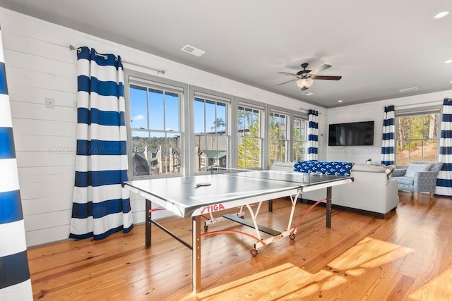 recreation room featuring ceiling fan, wood walls, and hardwood / wood-style flooring