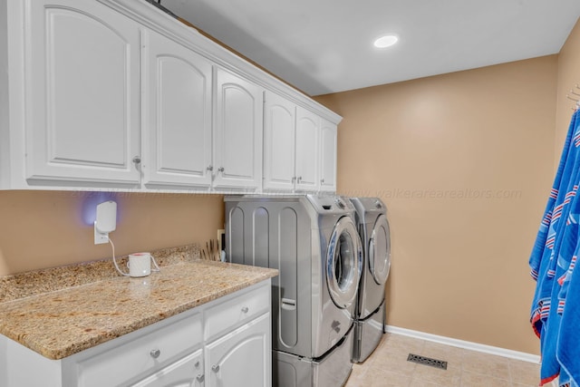 clothes washing area with cabinets, washing machine and dryer, and light tile patterned floors