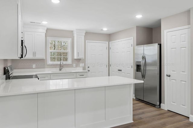 kitchen featuring stainless steel appliances, a peninsula, light countertops, white cabinetry, and a sink