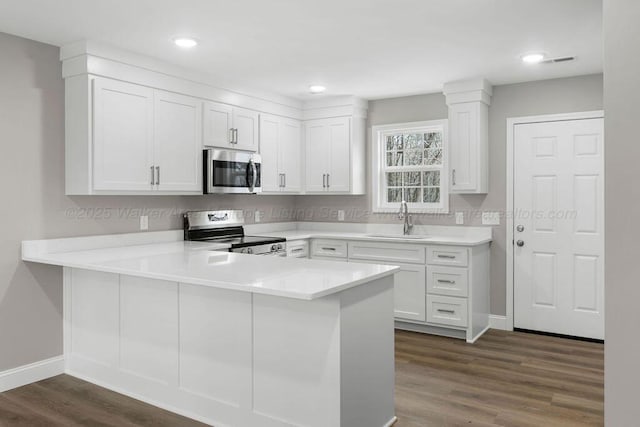 kitchen featuring appliances with stainless steel finishes, a peninsula, light countertops, white cabinetry, and a sink