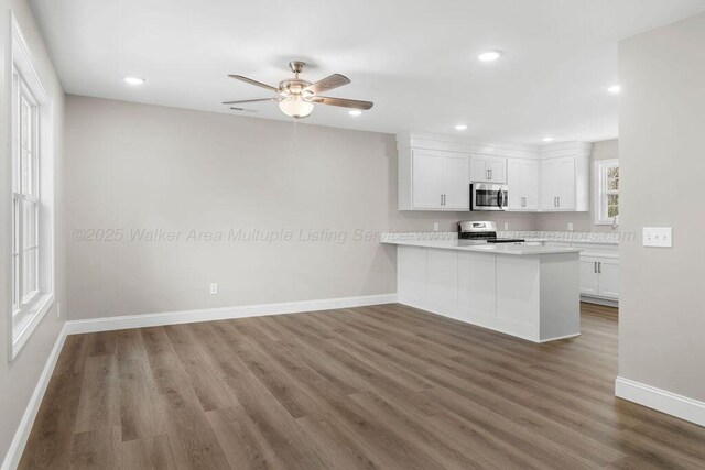 kitchen with a peninsula, dark wood-type flooring, white cabinetry, appliances with stainless steel finishes, and light countertops