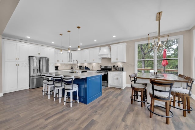 kitchen with appliances with stainless steel finishes, custom range hood, decorative light fixtures, hardwood / wood-style flooring, and white cabinets