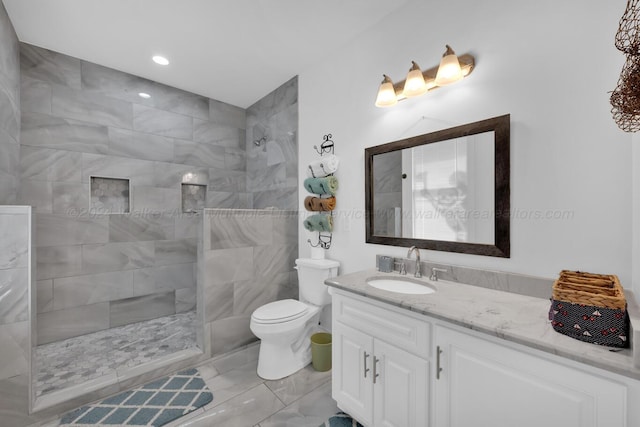 bathroom featuring a tile shower, vanity, and toilet