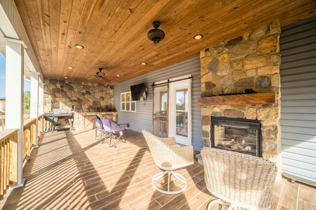 deck featuring area for grilling, an outdoor stone fireplace, and ceiling fan