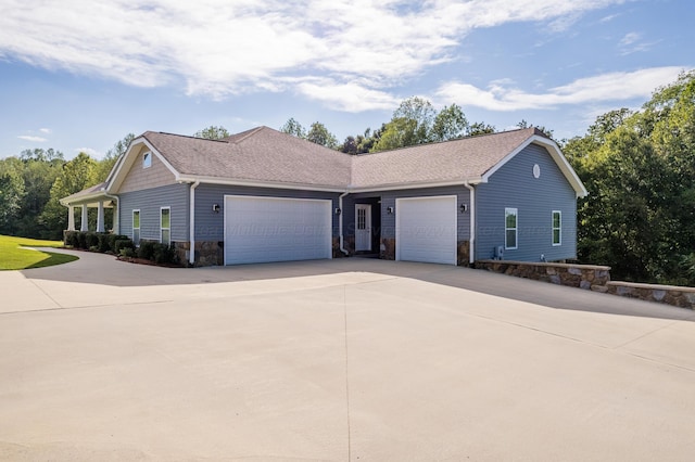 ranch-style home featuring stone siding, an attached garage, driveway, and roof with shingles