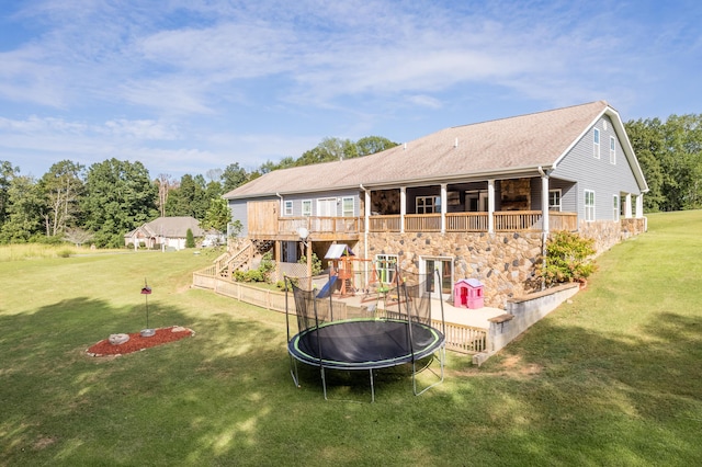 rear view of property with stone siding, a trampoline, a playground, a yard, and a shingled roof