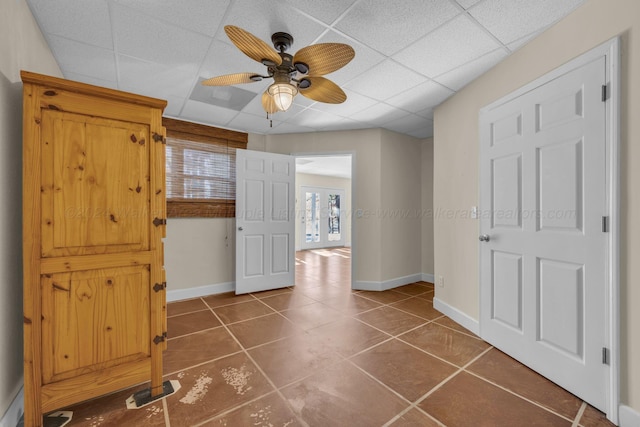 interior space with ceiling fan, a drop ceiling, and dark tile patterned flooring