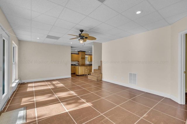 unfurnished living room with ceiling fan, a drop ceiling, and dark tile patterned flooring