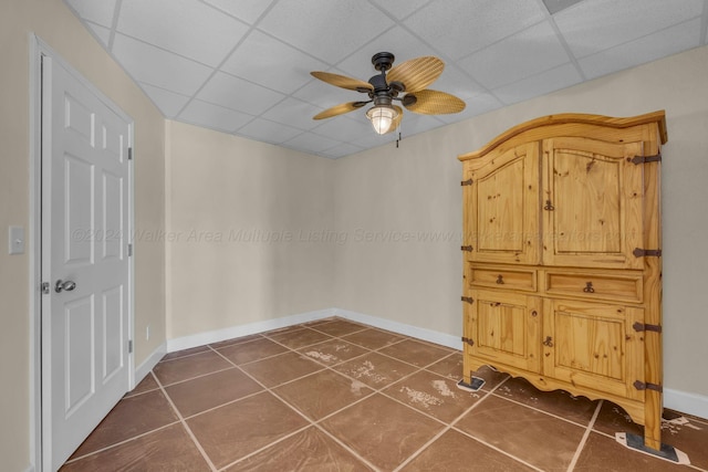 interior space with a drop ceiling, dark tile patterned flooring, and ceiling fan