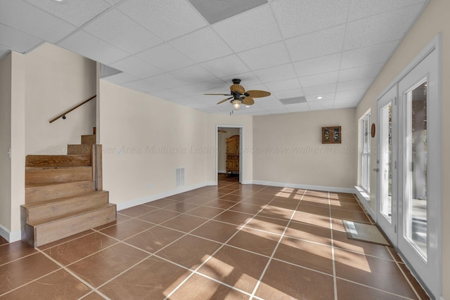 interior space with ceiling fan, a drop ceiling, and dark tile patterned floors