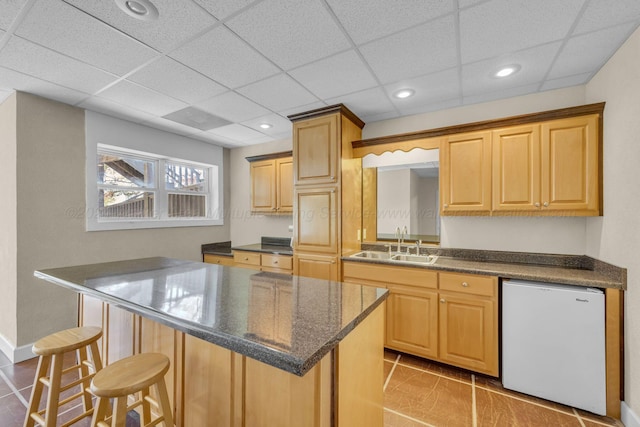 kitchen with light tile patterned floors, white fridge, a kitchen island, and sink