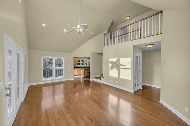 unfurnished living room featuring hardwood / wood-style flooring, ceiling fan, high vaulted ceiling, and french doors