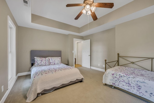 carpeted bedroom featuring ceiling fan and a tray ceiling