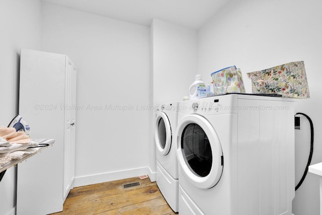 clothes washing area with washing machine and dryer and light wood-type flooring