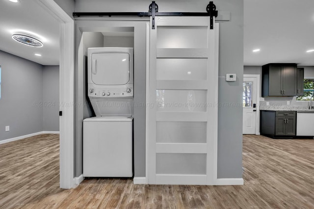 laundry room featuring a barn door, stacked washer and dryer, and light hardwood / wood-style floors