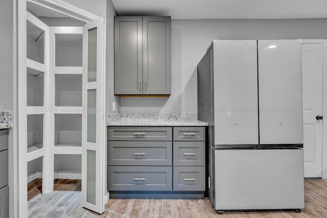 interior space with light stone countertops, light hardwood / wood-style floors, gray cabinets, and white fridge