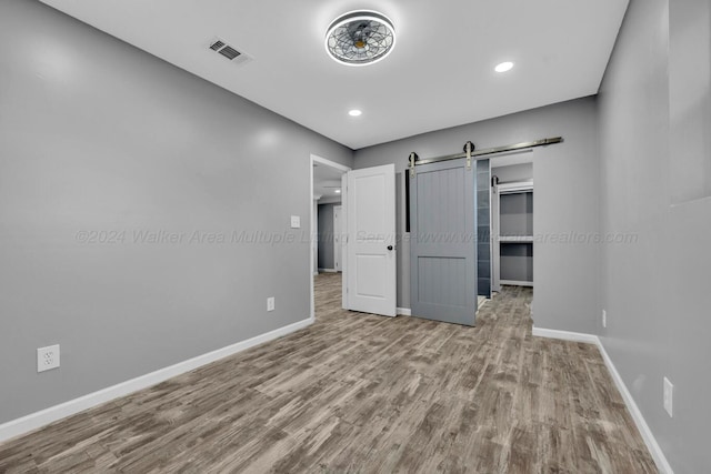 unfurnished bedroom featuring a barn door, light hardwood / wood-style floors, and a closet