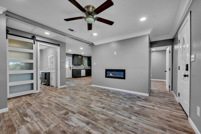 unfurnished living room featuring a barn door, ceiling fan, hardwood / wood-style floors, and ornamental molding