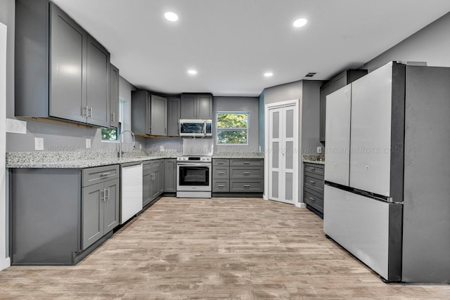 kitchen with light stone countertops, sink, stainless steel appliances, gray cabinets, and light wood-type flooring