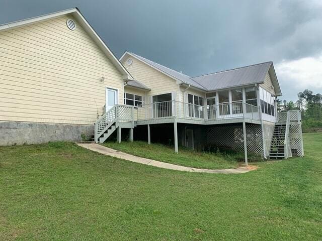 rear view of property featuring a sunroom, a deck, and a yard