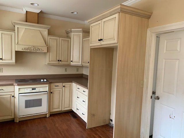 kitchen with custom range hood, crown molding, cream cabinetry, dark hardwood / wood-style floors, and oven