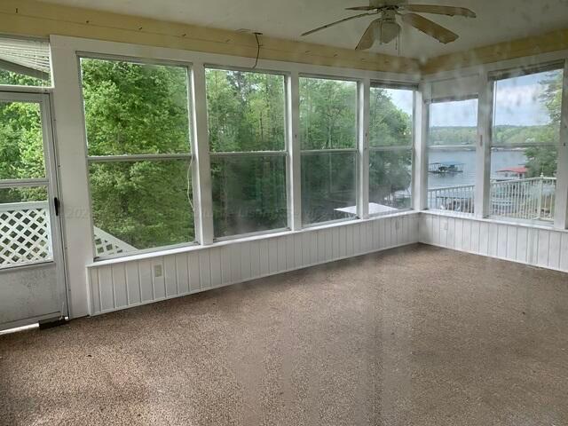 unfurnished sunroom with ceiling fan and a water view