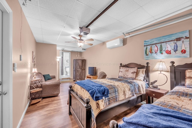 bedroom with light wood-type flooring, a wall unit AC, ceiling fan, and a paneled ceiling