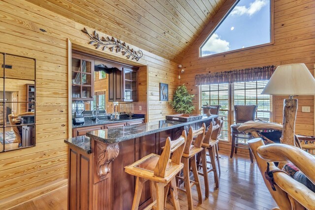 kitchen featuring high vaulted ceiling, wooden ceiling, dark stone countertops, hardwood / wood-style floors, and wood walls