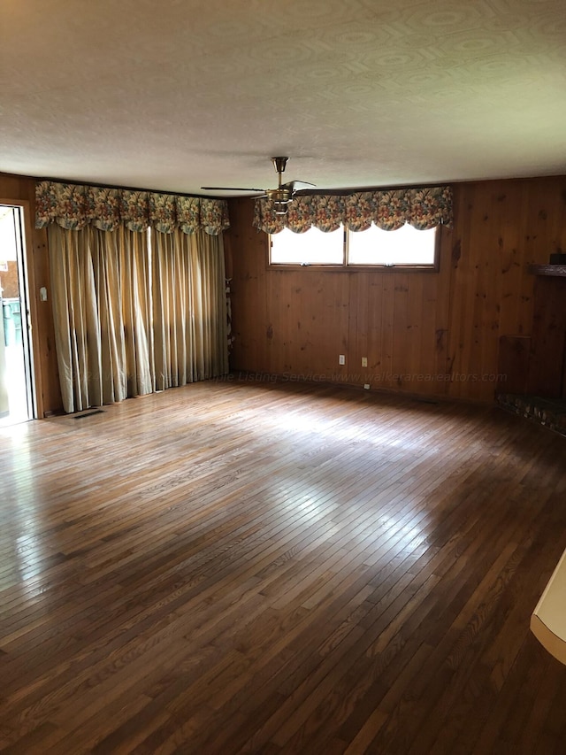 unfurnished room with ceiling fan, dark wood-type flooring, and wood walls