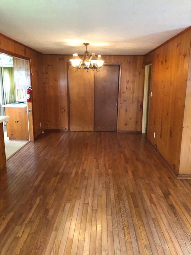 spare room featuring wood walls, dark wood-type flooring, and an inviting chandelier