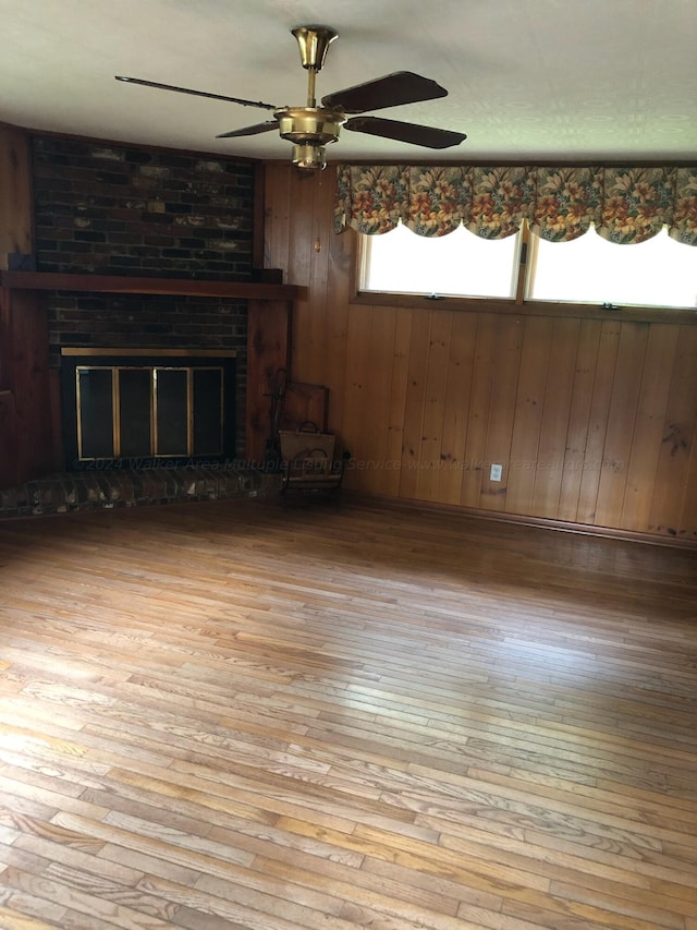 unfurnished living room featuring wooden walls, light hardwood / wood-style flooring, ceiling fan, and a brick fireplace