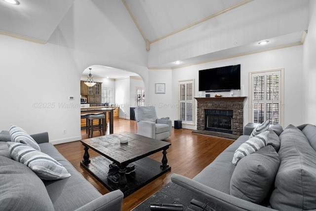 living area featuring dark wood-style floors, arched walkways, high vaulted ceiling, and ornamental molding