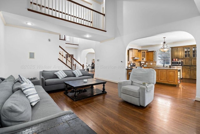 living area featuring arched walkways, dark wood-style flooring, baseboards, stairs, and crown molding