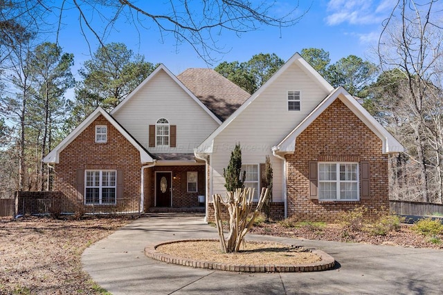 traditional-style home featuring driveway, brick siding, and roof with shingles