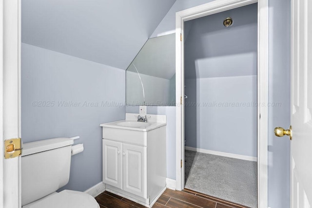 bathroom with lofted ceiling, toilet, wood finish floors, vanity, and baseboards