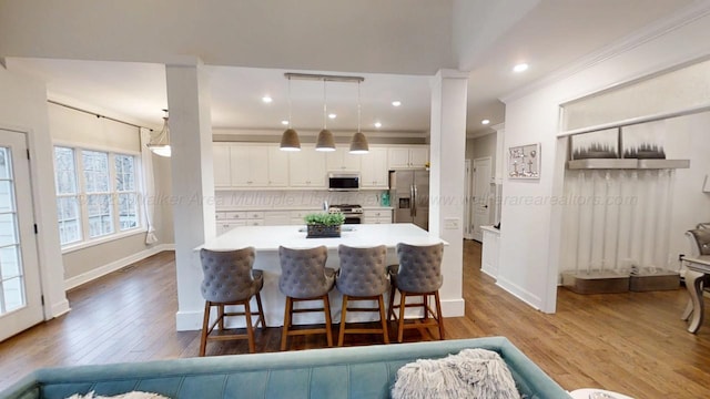 kitchen with a breakfast bar area, white cabinets, hanging light fixtures, appliances with stainless steel finishes, and light countertops