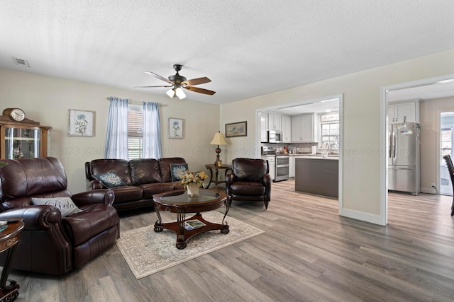 living room featuring ceiling fan, a healthy amount of sunlight, light hardwood / wood-style floors, and a textured ceiling