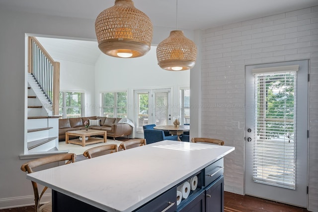 kitchen featuring dark wood-type flooring, blue cabinetry, hanging light fixtures, a center island, and brick wall