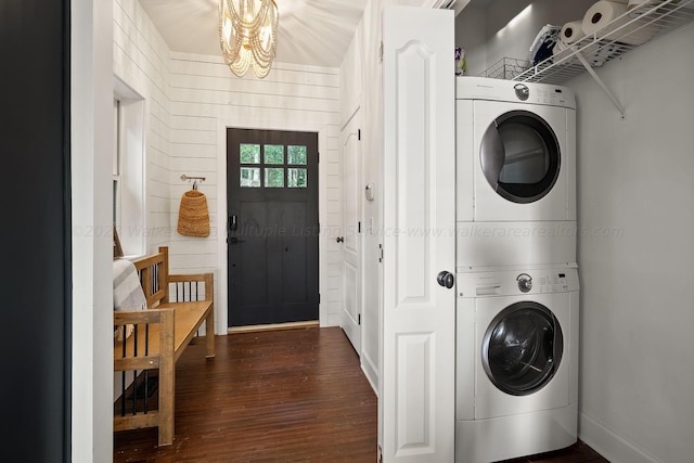 washroom with an inviting chandelier, stacked washer and clothes dryer, dark hardwood / wood-style flooring, and wood walls